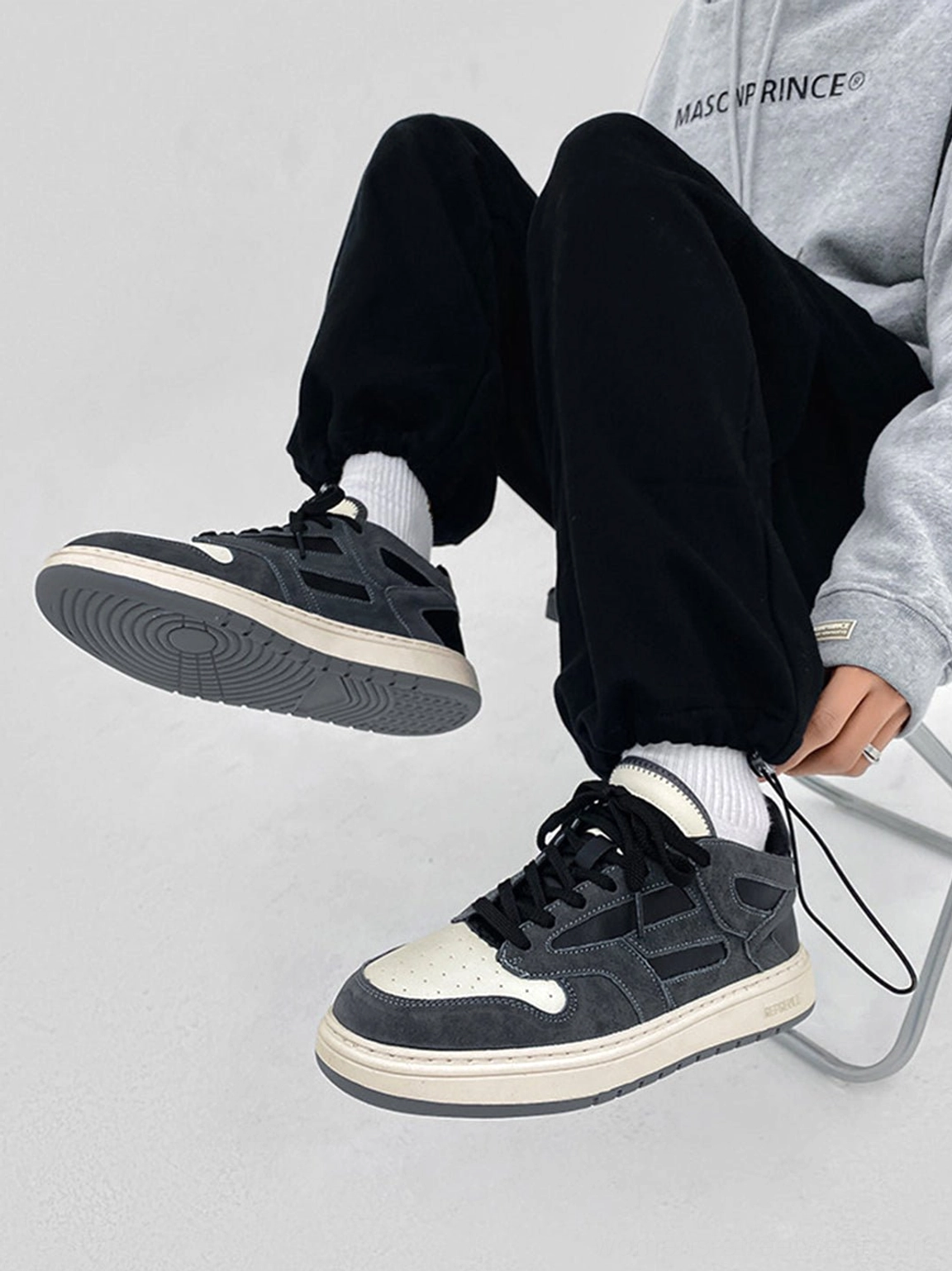 Model wearing black suede-look low-top sneakers with white crew socks black joggers and gray hoodie streetwear outfit