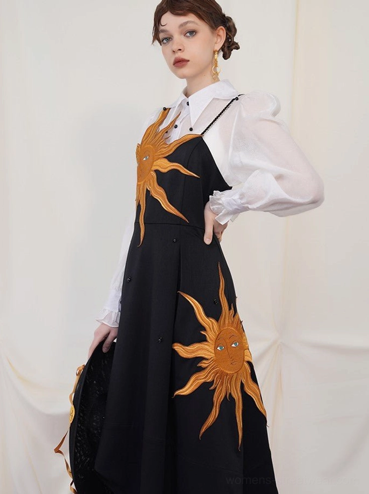 Side view of a black sun embroidered slip dress styled with a sheer white blouse and matching celestial handbag