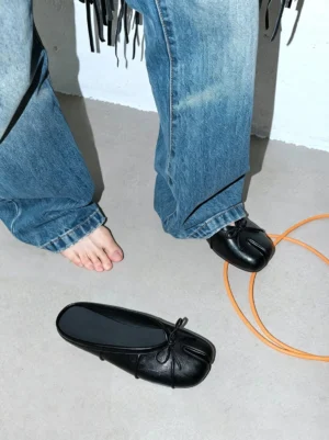 Model wearing black split tabi toe bow mules with relaxed baggy blue jeans in a casual streetwear outfit
