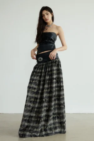 Front full body view of a black tartan plaid maxi skirt styled with a strapless faux leather corset top and silver hardware in a minimalist studio