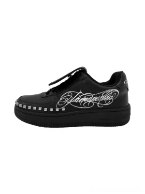 Black tattoo style low top chunky leather sneakers with white cursive side artwork, studded midsole trim and lace up streetwear design