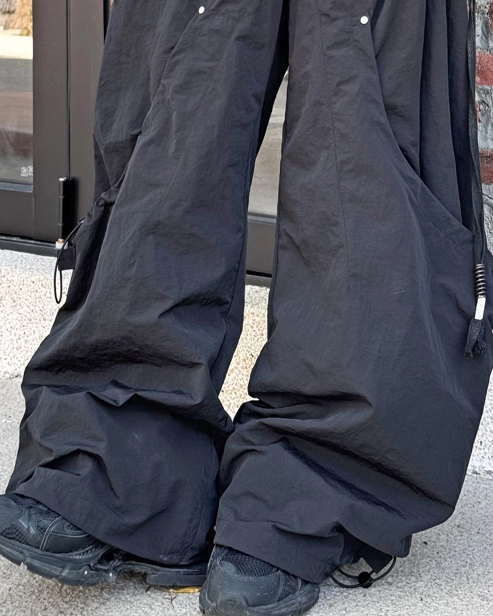 Black technical cargo pants with wide legs drawstring waist oversized pockets and industrial streetwear detailing