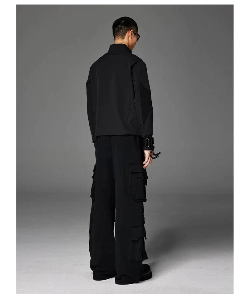 Back three-quarter view of a male model wearing a black stand-collar softshell streetwear jacket styled with cargo pants and tactical wrist accessories