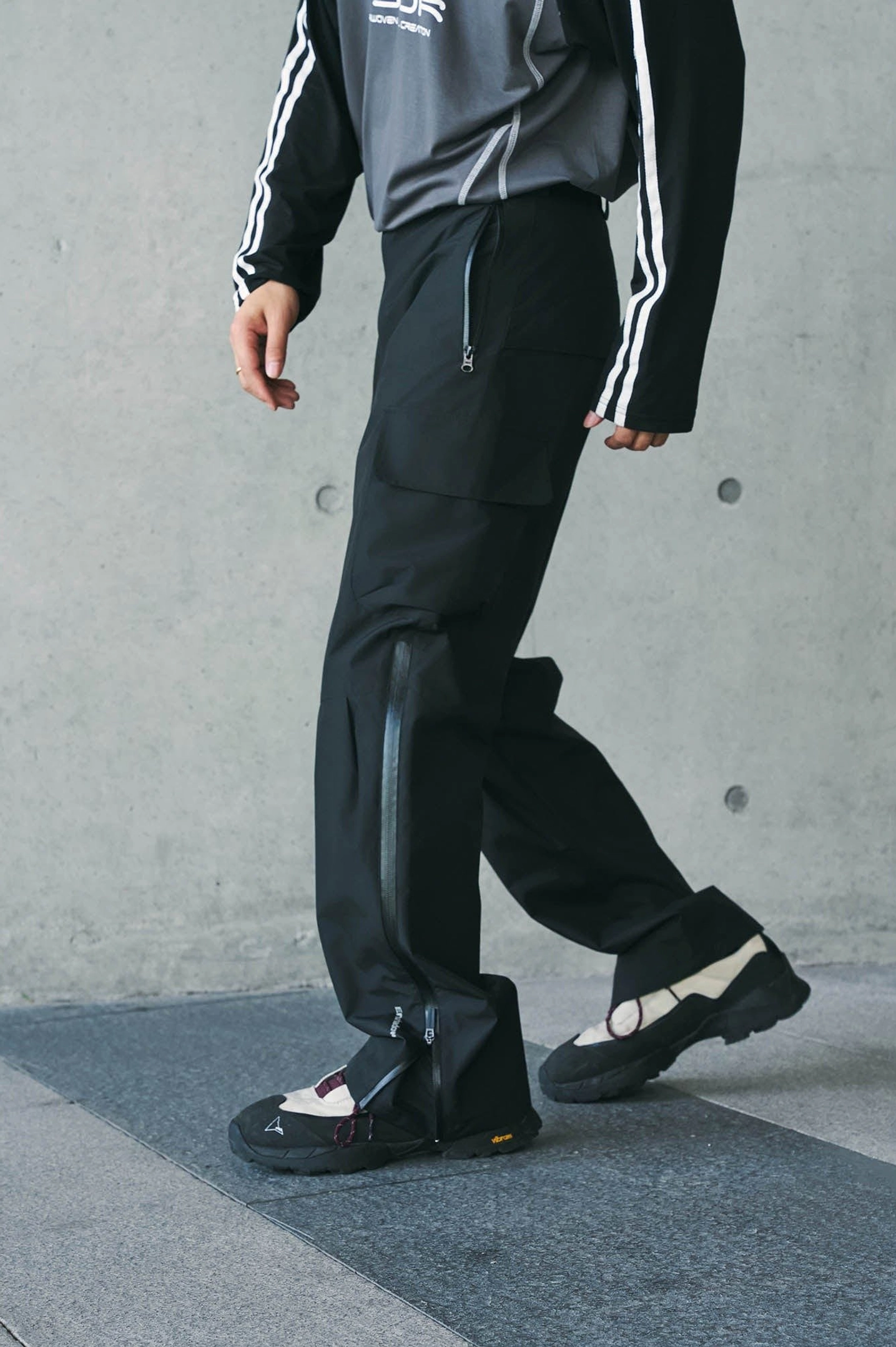 Black techwear waterproof cargo pants shown in a side walking view with ankle zipper detail, thigh pocket, and smooth technical fabric