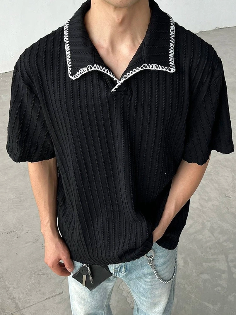 Black textured short sleeve polo shirt with open collar and contrast white stitching styled with light wash jeans