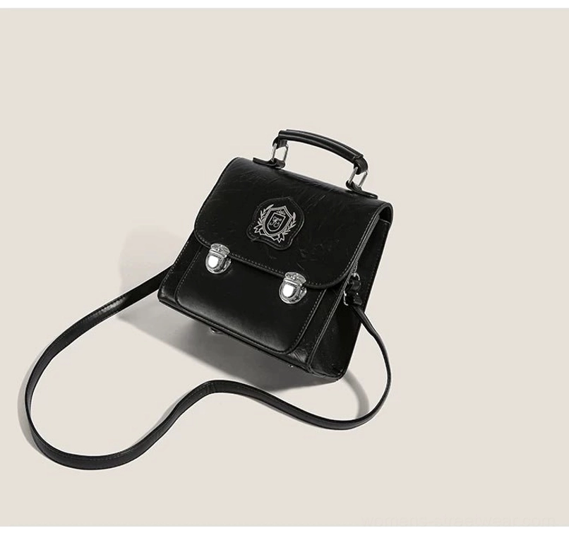 Side view of black textured PU mini satchel crossbody bag with structured silhouette, crest patch, and silver-tone hardware