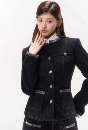 Close-up of black textured tweed blazer featuring fitted waist metallic buttons braided pocket trim and structured stand collar