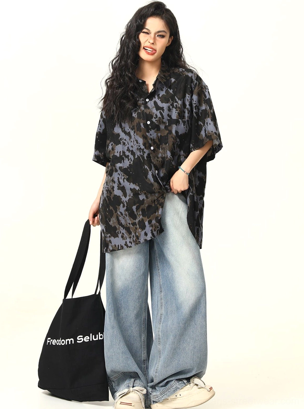 Side view of black tie-dye oversized short-sleeve shirt with hip-covering length and wide-leg jeans
