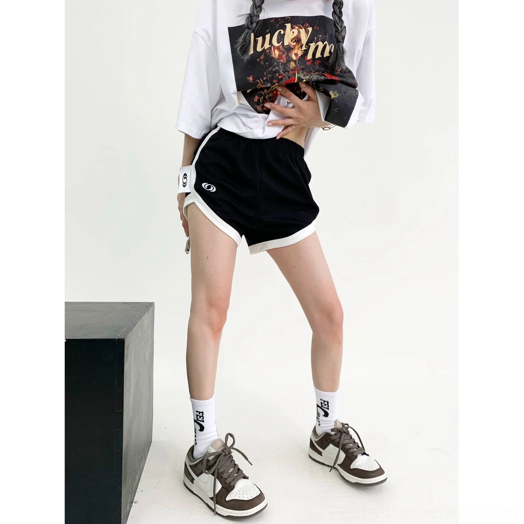 Standing lower body view of black track shorts with white piping around the leg openings, standard short length, and graphic front emblem