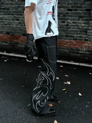 Side view of dark black wide leg denim jeans featuring white tribal tattoo flame embroidery, classic rear pocket, and oversized streetwear silhouette