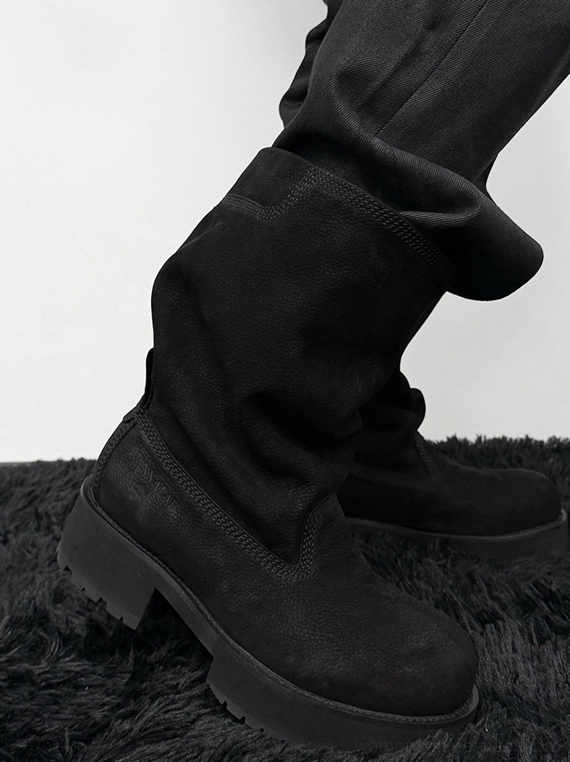 Side profile of black tumbled leather mid-calf platform boots styled with wide-leg dark trousers and a relaxed fold-over shaft
