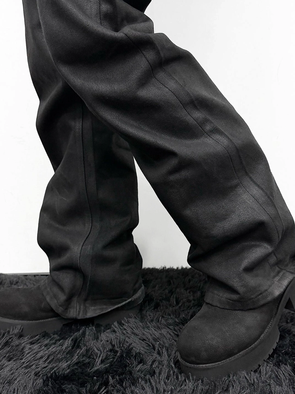 Low front view of black tumbled leather slouch boots with loose trousers, rounded toe shapes, and substantial platform-style soles