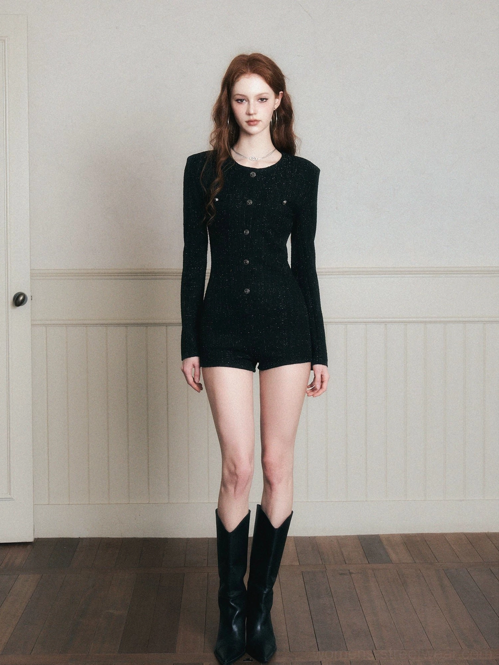 Front full-body view of a black tweed romper featuring a round crew neck, long sleeves, decorative button front, fitted waist, and sleek streetwear silhouette