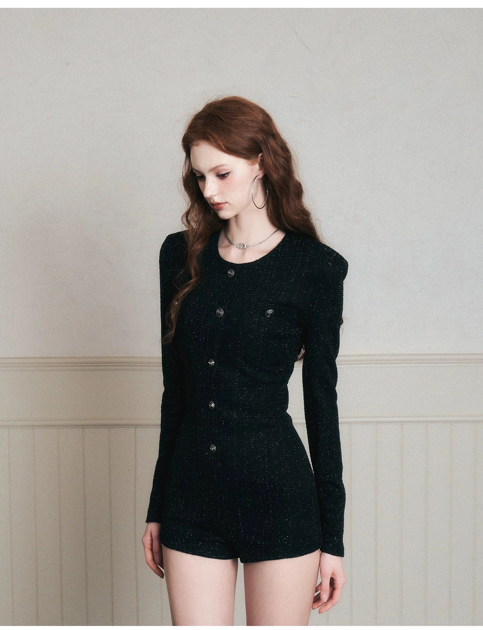 Close-up torso view of a black tweed romper with a round crew neckline, decorative front button row, fitted bodice, long sleeves, and subtle fabric texture