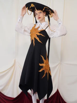 Front view of a black twilight sun embroidered asymmetric slip maxi dress styled with a sheer white blouse and wide brim hat