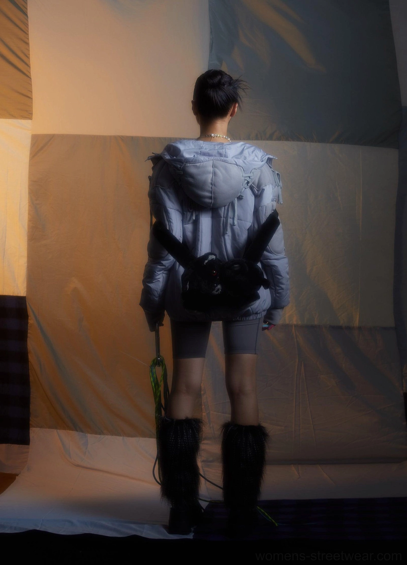 Female model wearing black twin evil bear faux fur mini backpack on the back with a light blue puffer jacket and fuzzy boots