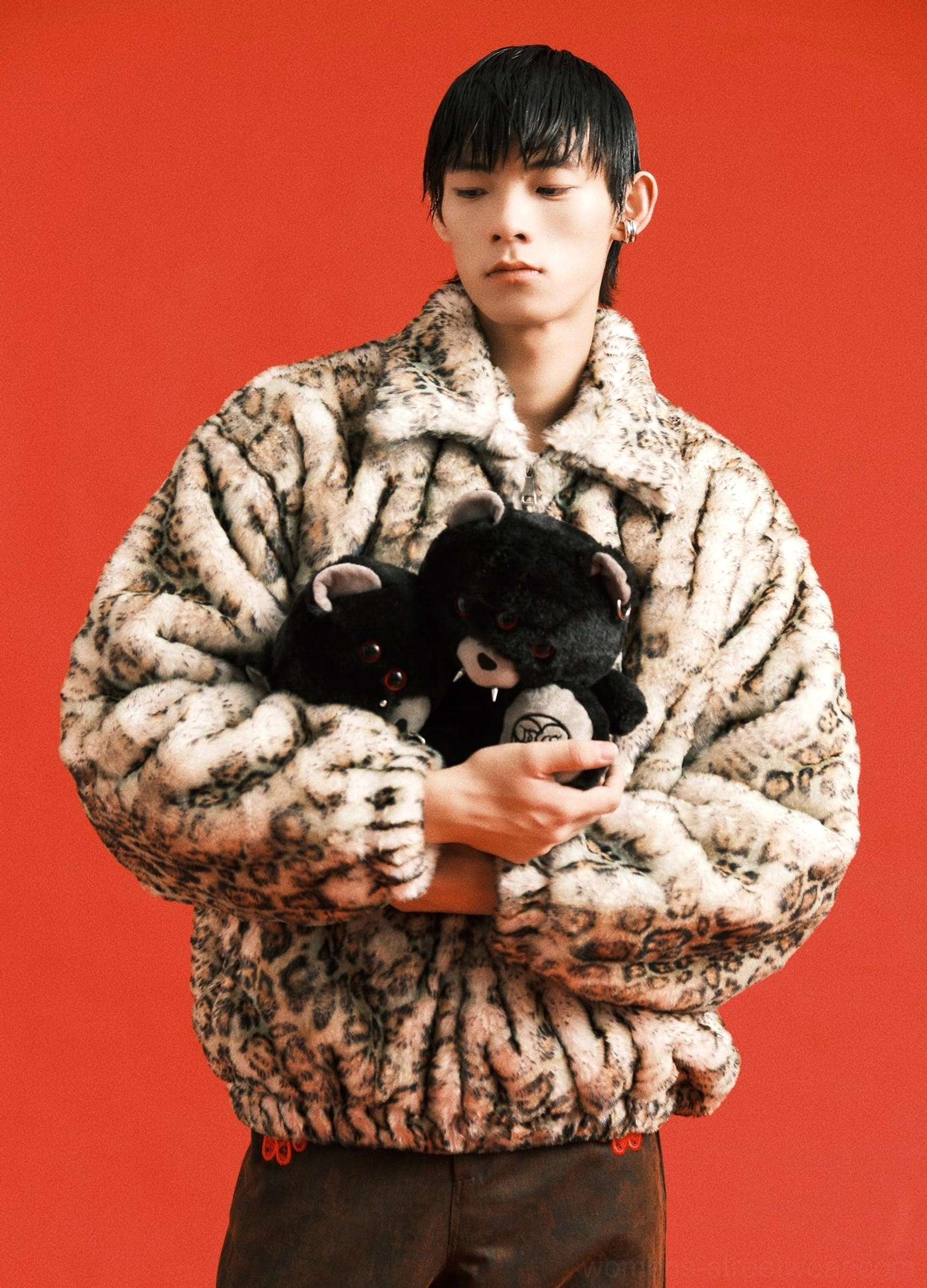 Male model holding black twin evil bear faux fur mini backpack with red eyes and metal-look piercings in a red studio