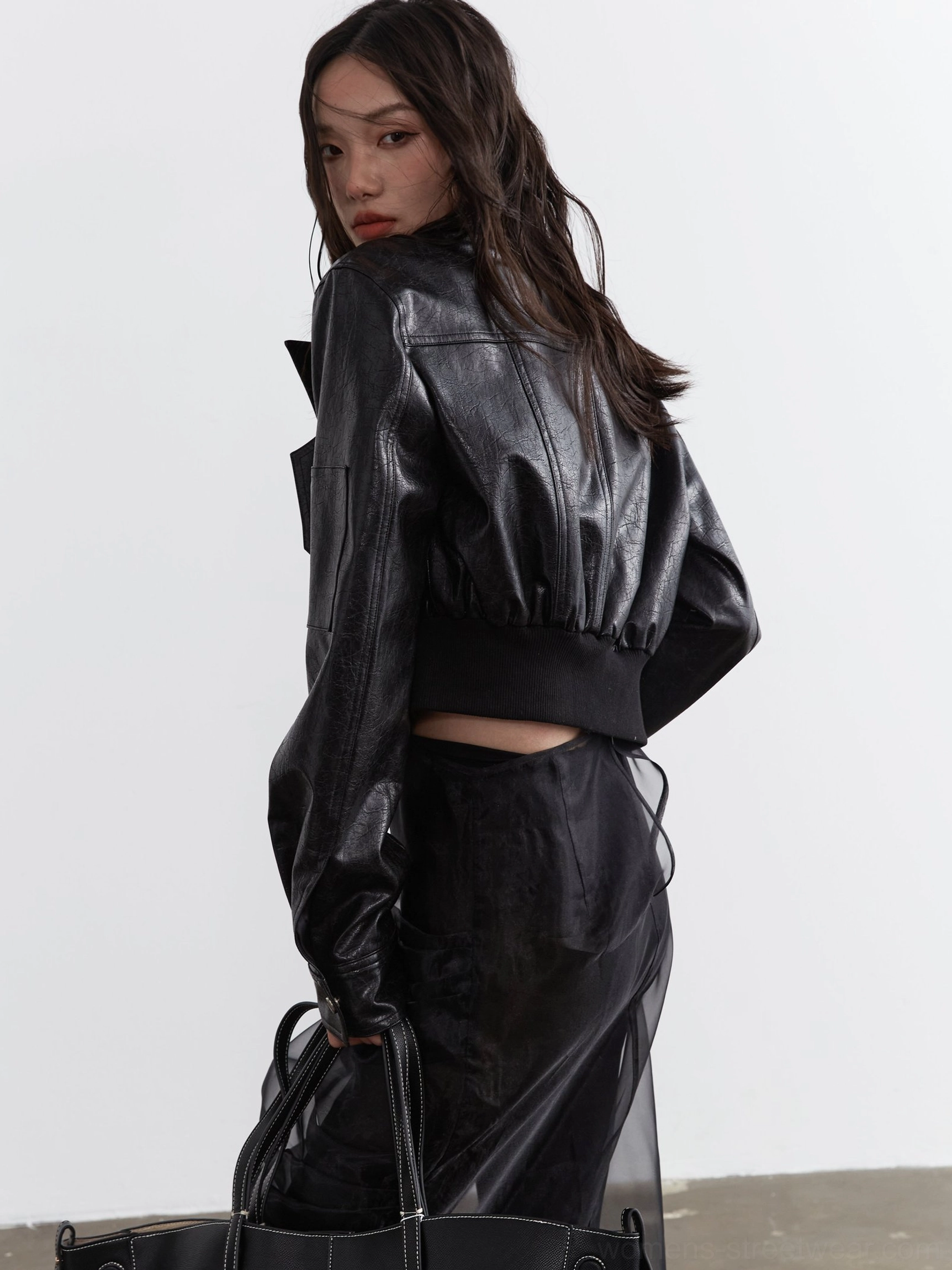 Back three-quarter view of a black ultra-cropped faux leather biker jacket showing its clean back silhouette, ribbed waist hem, and streamlined sleeve cuffs