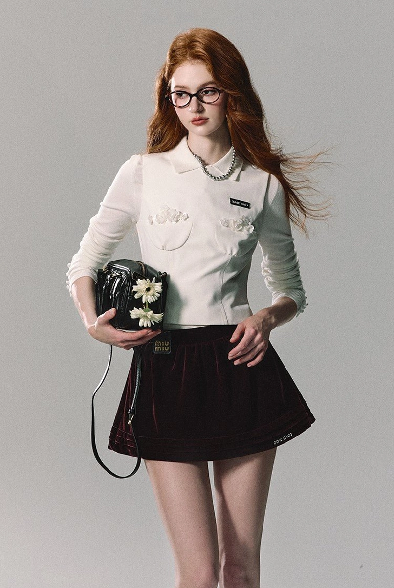 Black velvet A-line mini skirt styled with a white cropped ruffled polo shirt and pearl jewelry