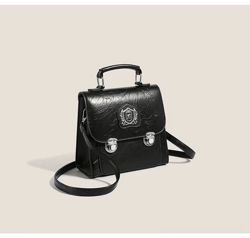 Black vintage-inspired mini crossbody satchel with shield crest detail, dual silver buckle accents, and detachable long strap