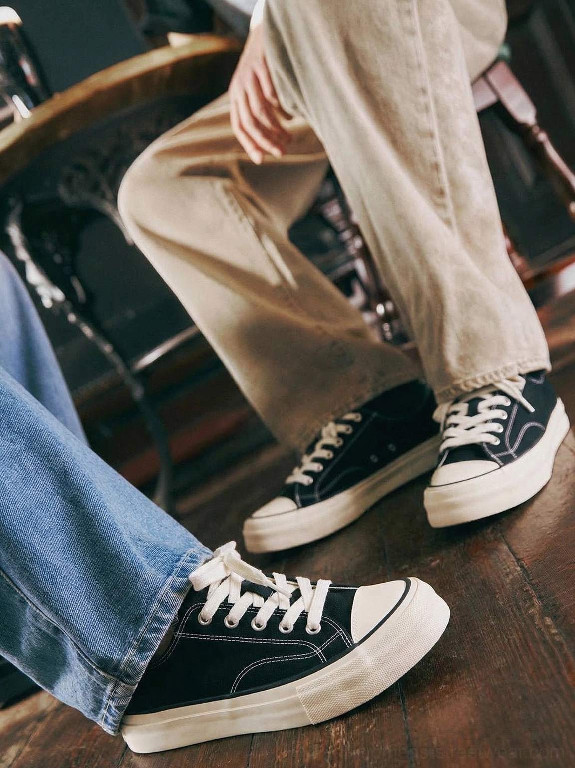 Two people wearing black vulcanized canvas platform low-top sneakers with jeans and khaki trousers in a vintage indoor setting