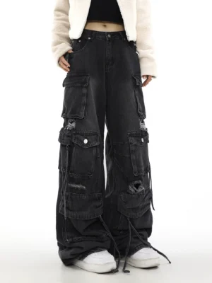 Front low-angle model view of black washed distressed wide-leg cargo jeans with stacked flap pockets and drawstring hems