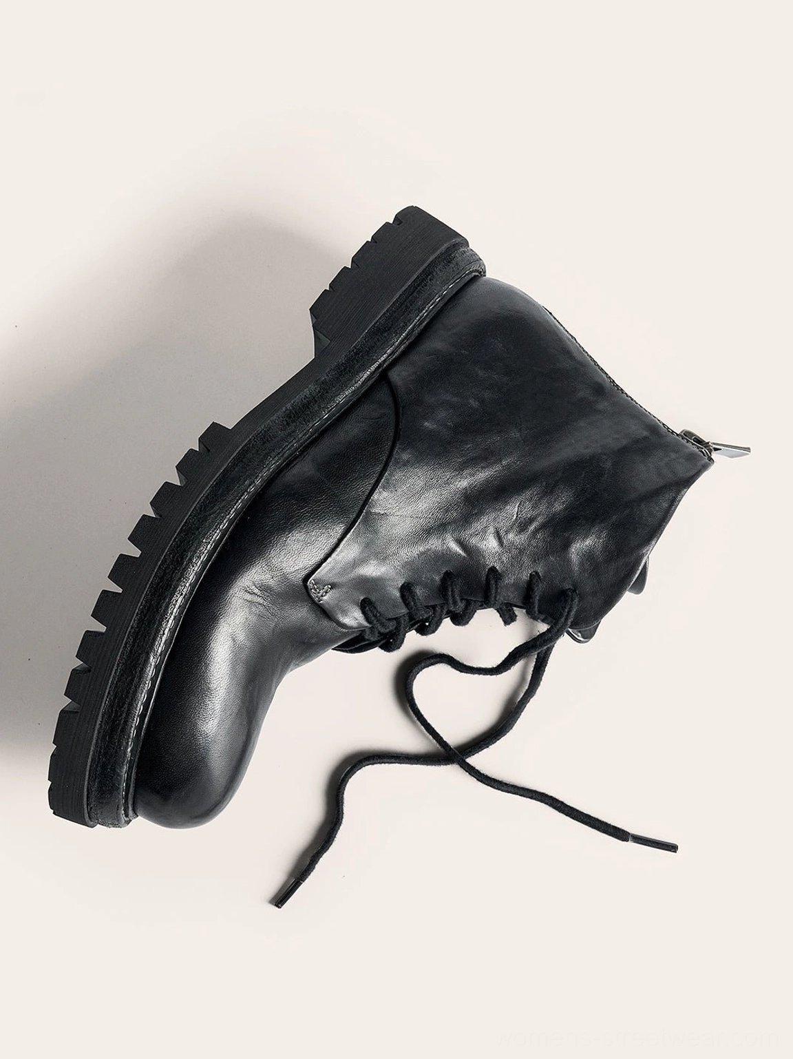 Close side view of a black washed horsehide combat boot showing the rear zipper, loose laces, vintage leather grain, and rugged lug tread