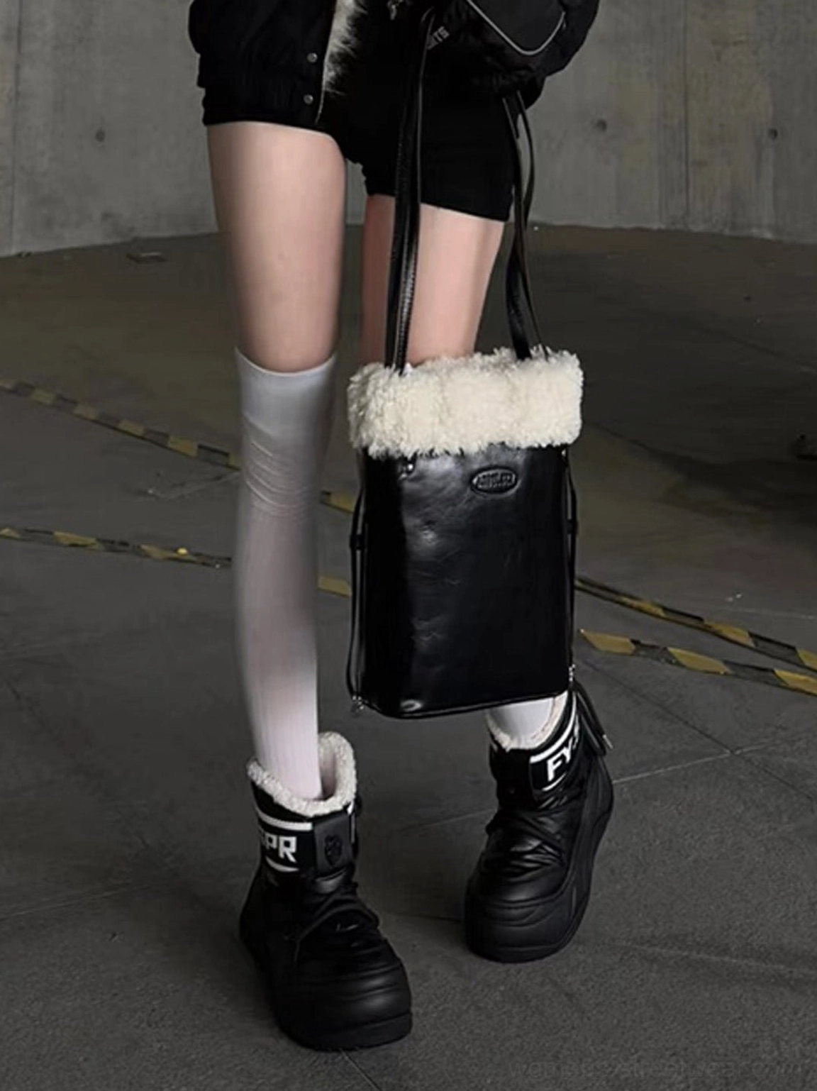 Front view of black water-resistant chunky moon boots styled with white thigh-high socks and a black streetwear outfit