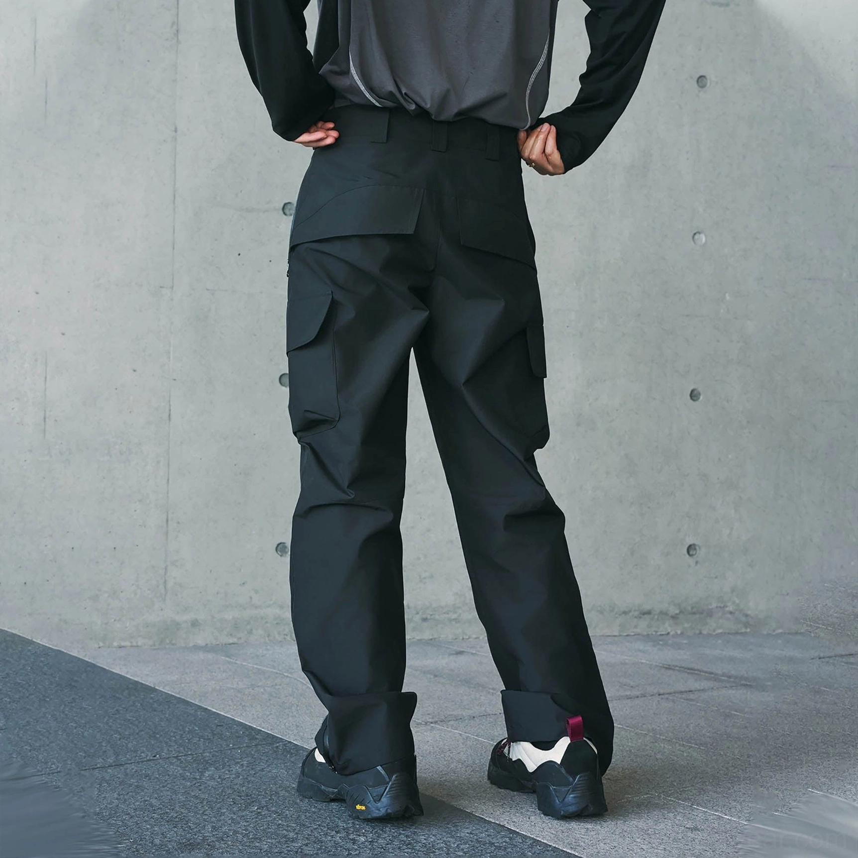 Black waterproof cargo pants shown from the back with rear storage pockets, thigh cargo pockets, and a clean loose straight-leg design