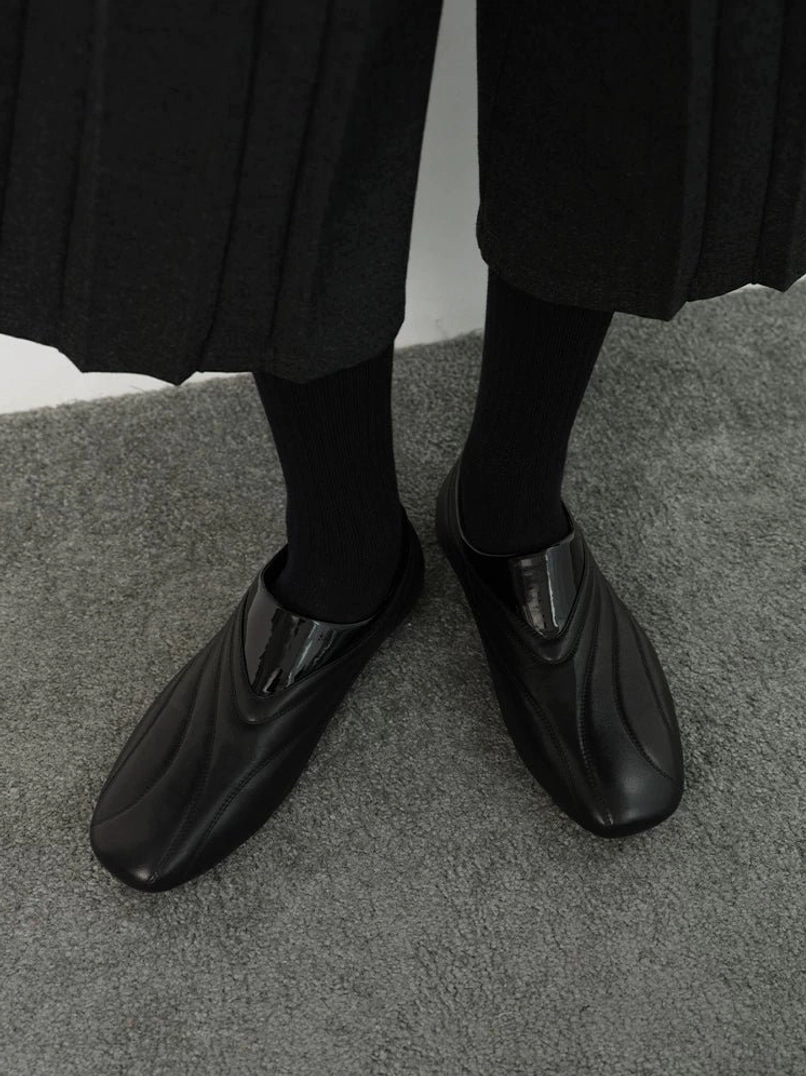 Black wave seam low-profile leather slip-on streetwear shoes worn with black socks and a midi skirt on indoor carpet
