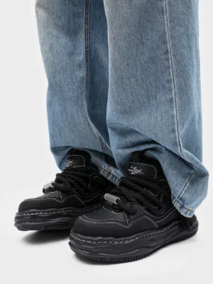 Pair of black wavy platform sneakers styled with loose blue denim jeans and visible contrast stitching