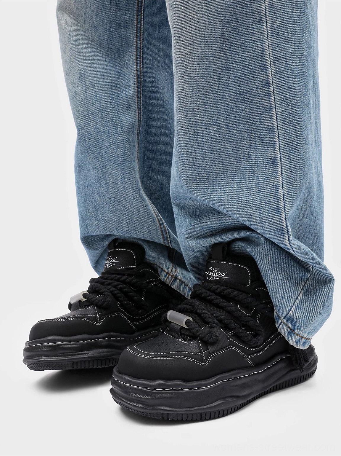 Pair of black wavy platform sneakers styled with loose blue denim jeans and visible contrast stitching