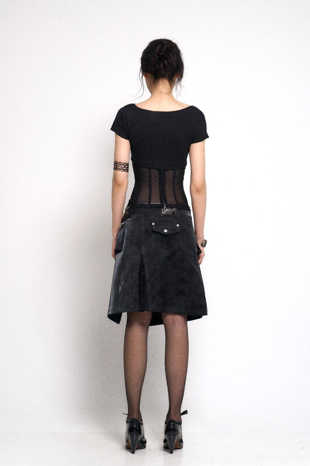 Back view of black weathered gothic mini skirt with pleated asymmetric hem and rear utility pocket