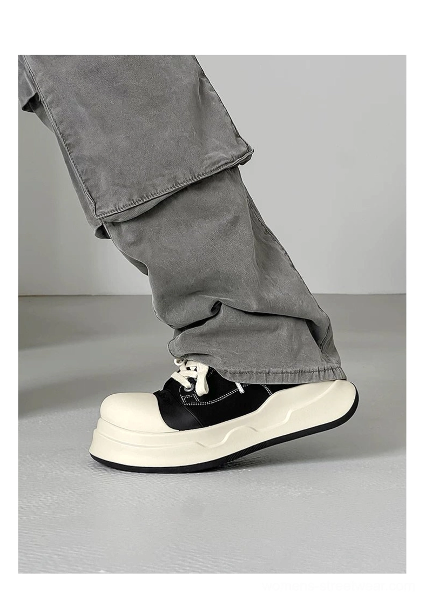 Side profile of black and white chunky round toe platform sneakers worn with grey cargo pants, showing the curved sole and oversized toe cap