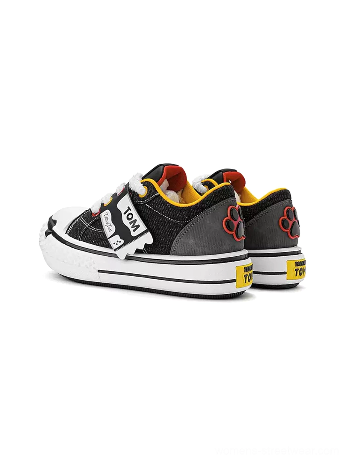 Rear three-quarter view of black and white chunky streetwear sneakers showing the paw print heel detail and yellow heel tab