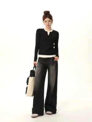 Full-body front view of a woman wearing a black and white color-block long-sleeve knit sweater with contrast collar and hem, dark wide-leg jeans, flat shoes, and a two-tone handbag in a Korean streetwear outfit