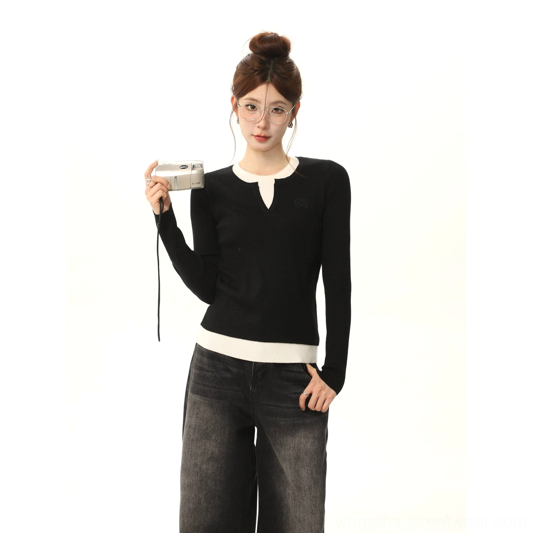Upper-body view of a woman wearing a black and white color-block long-sleeve sweater with clean round collar and hem contrast, paired with dark denim and a vintage film camera