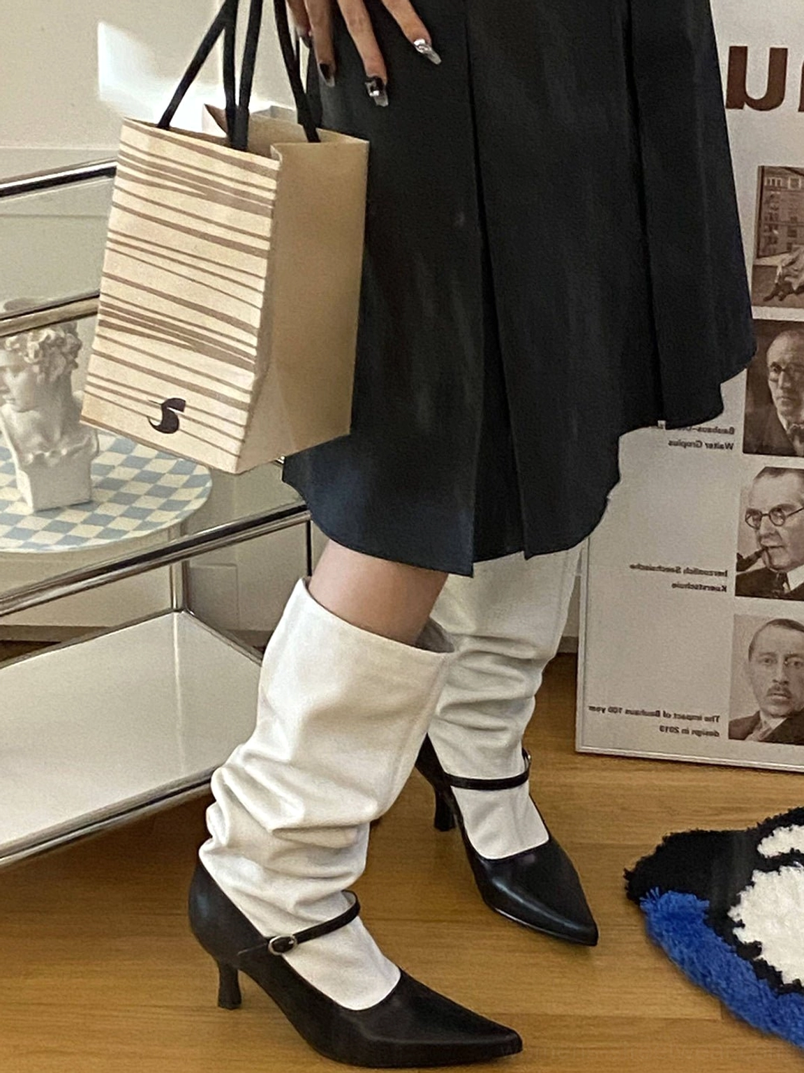 Front view of matching black and white color-block knee-high boots worn with a black pleated skirt and modern streetwear outfit