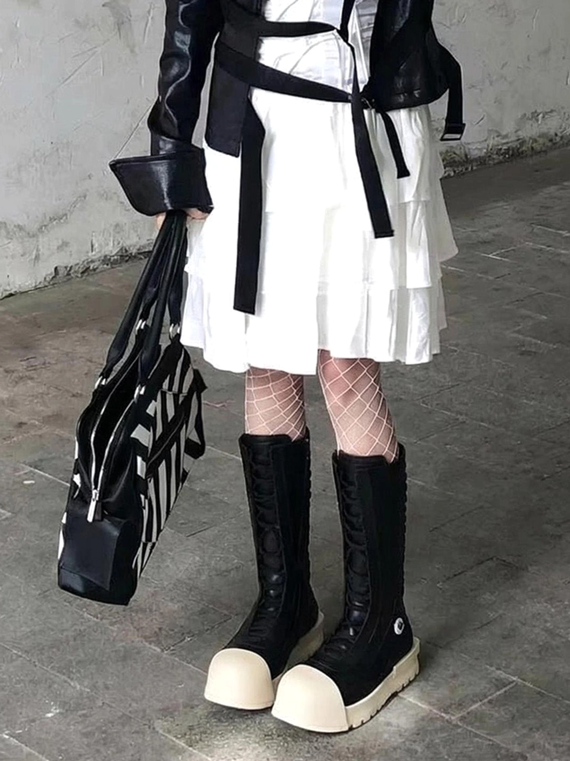 Full lower-body outfit featuring black and white contrast toe platform boots, fishnet tights, ruffled dress, cropped leather jacket, and striped handbag