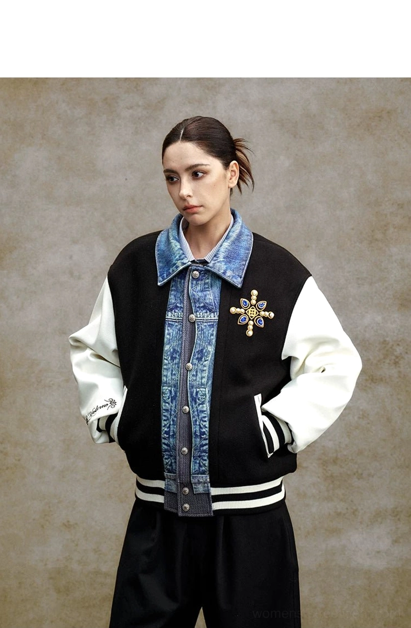 Black and white denim panel varsity bomber jacket front view showing chest embroidery, striped ribbed cuffs, striped hem, and side pockets