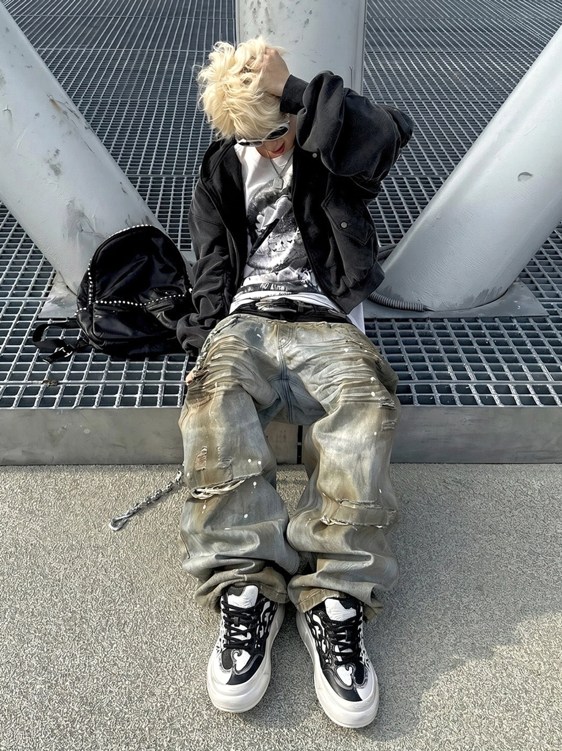 Model wearing black and white flame platform sneakers with wide leg jeans in a Y2K streetwear outfit on an industrial metal platform