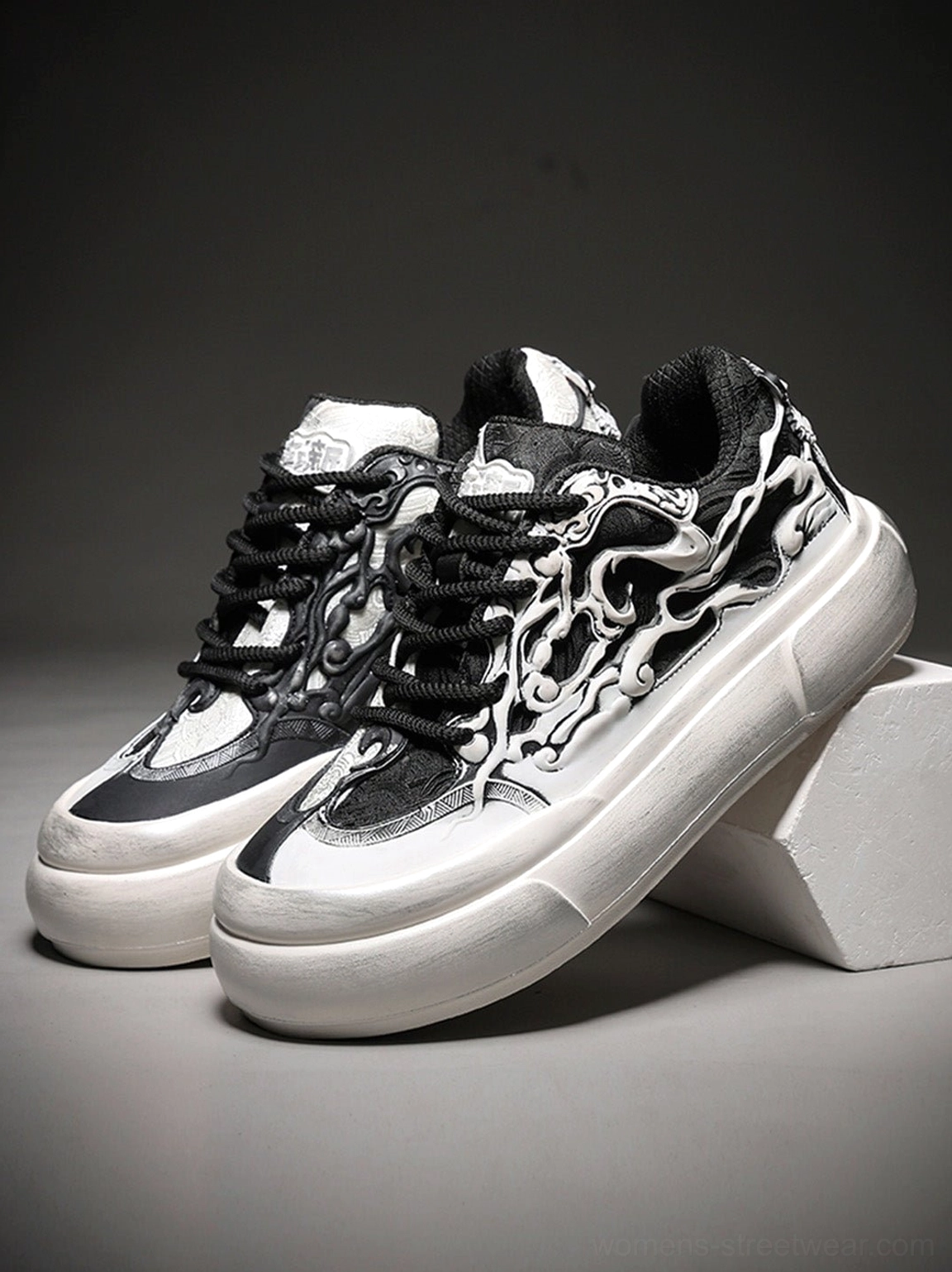 Pair of black and white flame skull platform sneakers displayed against a dark studio background with thick white platform soles