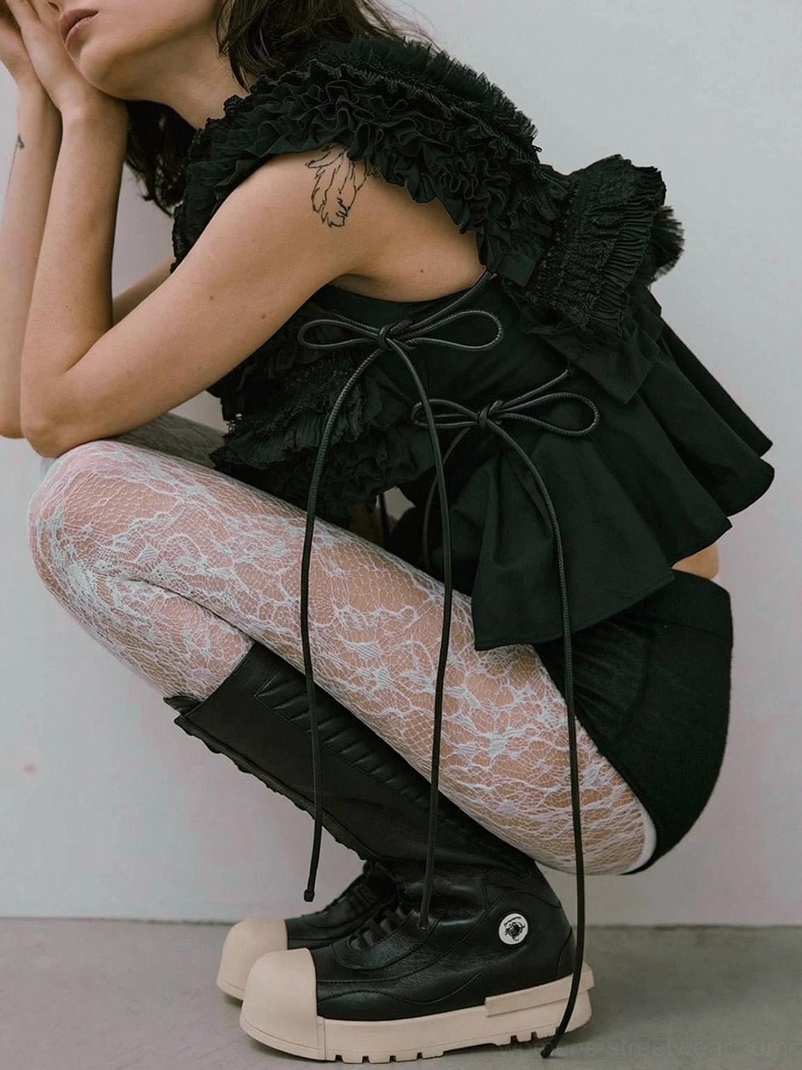 Female model wearing black and white mid-calf platform boots with fishnet tights and a ruffled black outfit in an alternative streetwear studio look