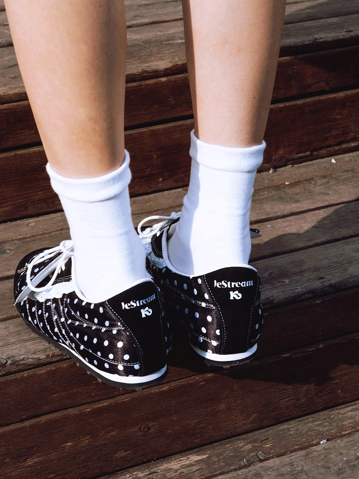 Back overhead close-up of black and white polka dot ballet flats with ruffled lace trim worn with white ankle socks