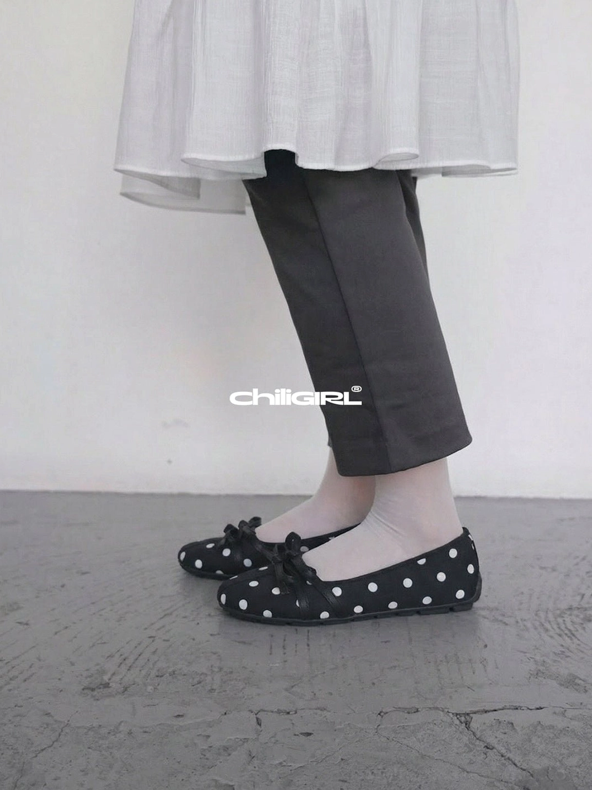 Black and white polka dot Mary Jane flats with front bows styled with white socks and dark grey tailored trousers