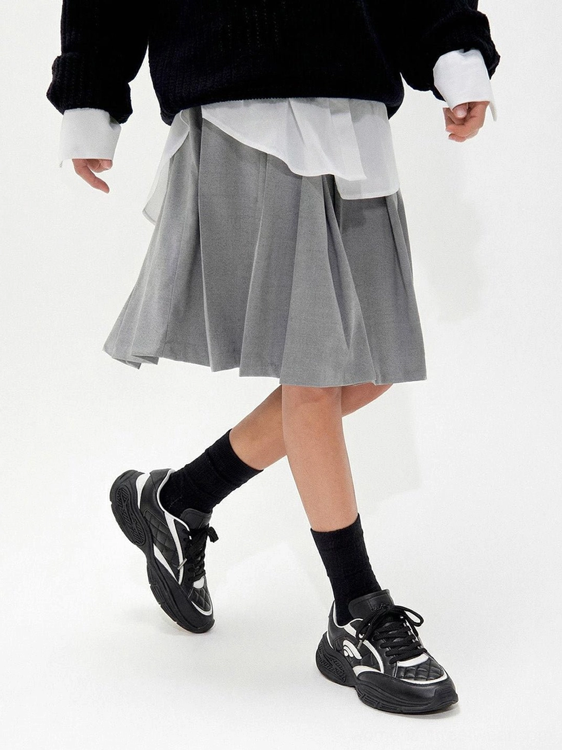 Black and white low-profile sport sneakers worn with a cropped knit top grey pleated skirt and black socks