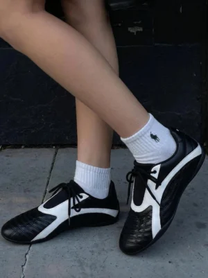 Black and white quilted toe flat sole streetwear sneakers worn outdoors with white crew socks on concrete pavement