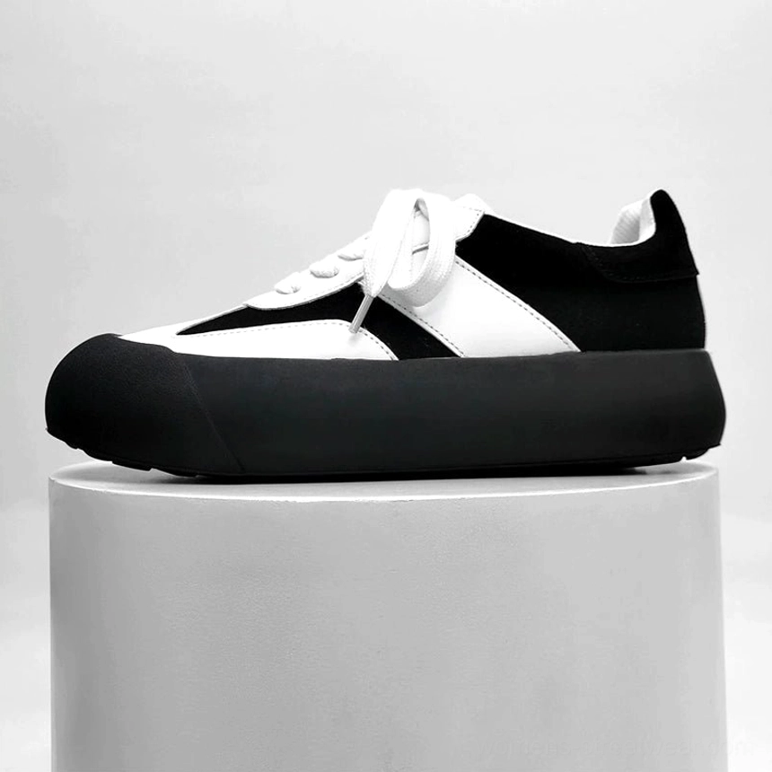 Black and white retro chunky sneakers displayed on a studio pedestal showing suede contrast panels and thick platform midsole