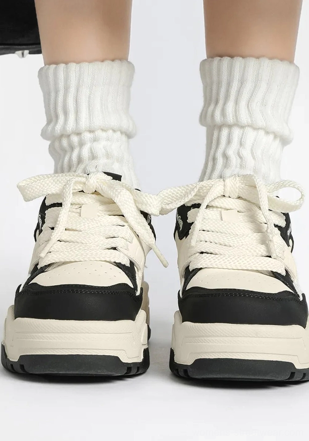 Front view of black and white retro platform sneakers with wide flat laces, black toe caps, contrasting sole trim, and thick socks