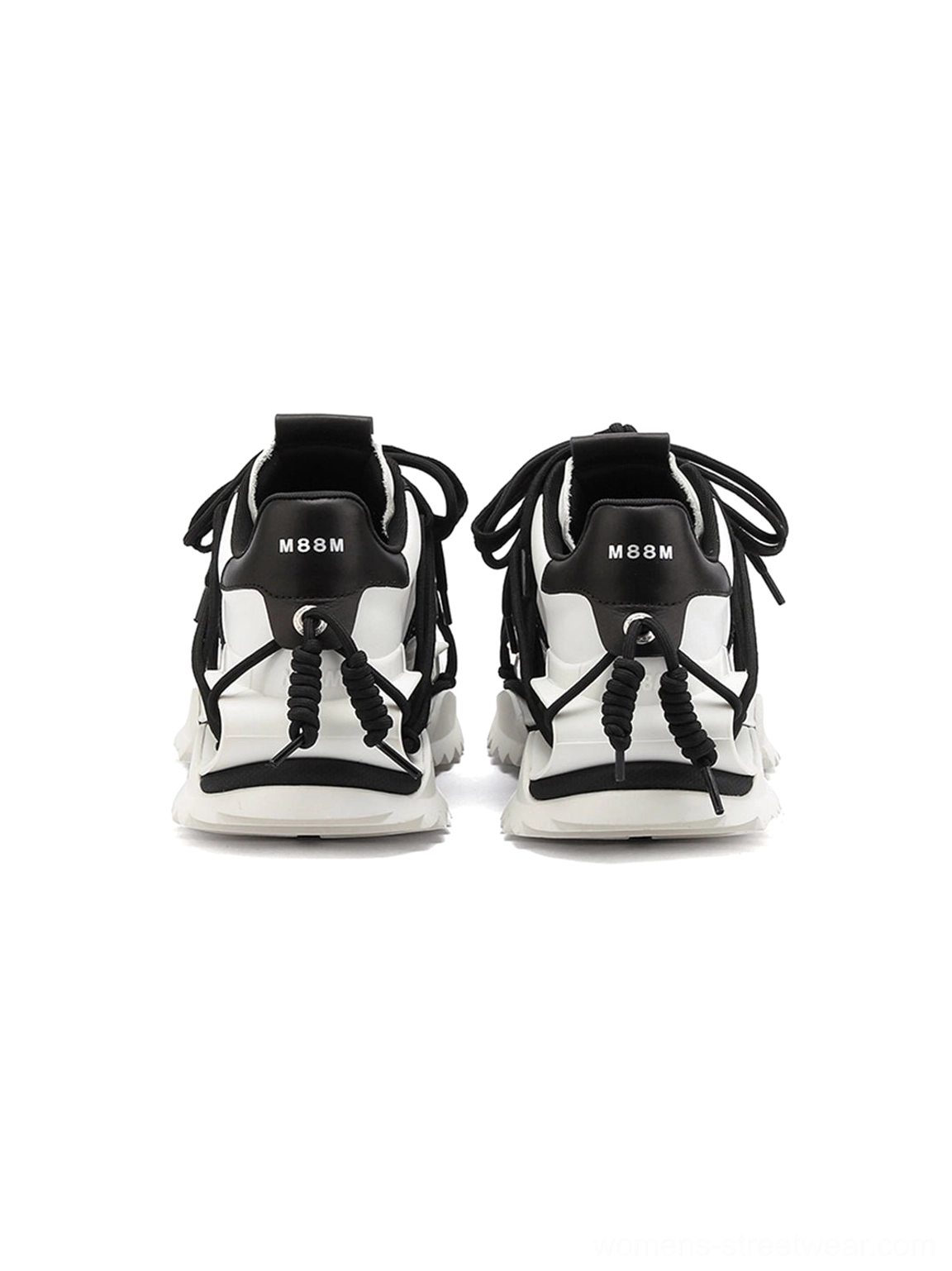 Close rear view of black and white sculpted sole sneakers showing decorative heel cords, pull tab construction, and rugged chunky outsole details